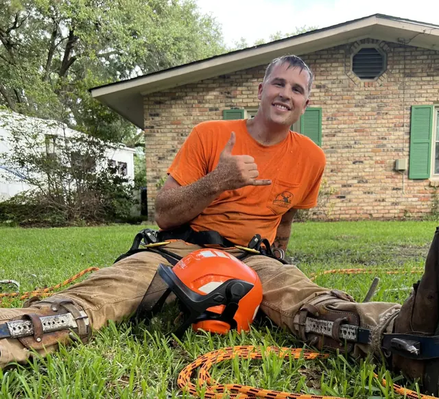 Dave Lau, owner of Log Hog Tree Service, smiling in a customer's yard with his climbing gear